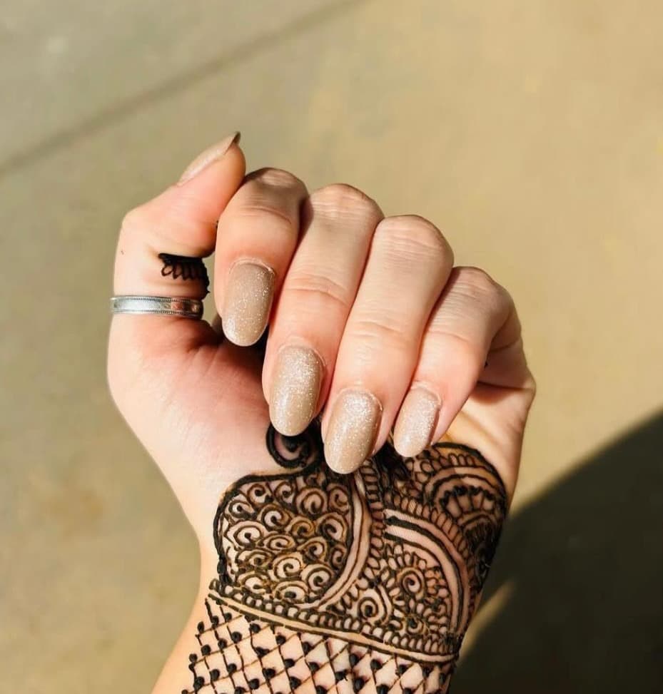 Soft nude shimmer manicure styled alongside intricate bridal henna
